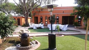 Un patio con una fuente, una zona de estar al aire libre techada y un edificio con fachada roja.