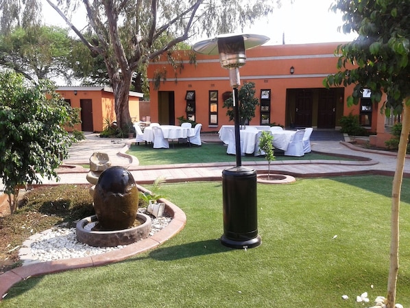 A courtyard with a fountain, a covered outdoor seating area, and a building with a red facade.
