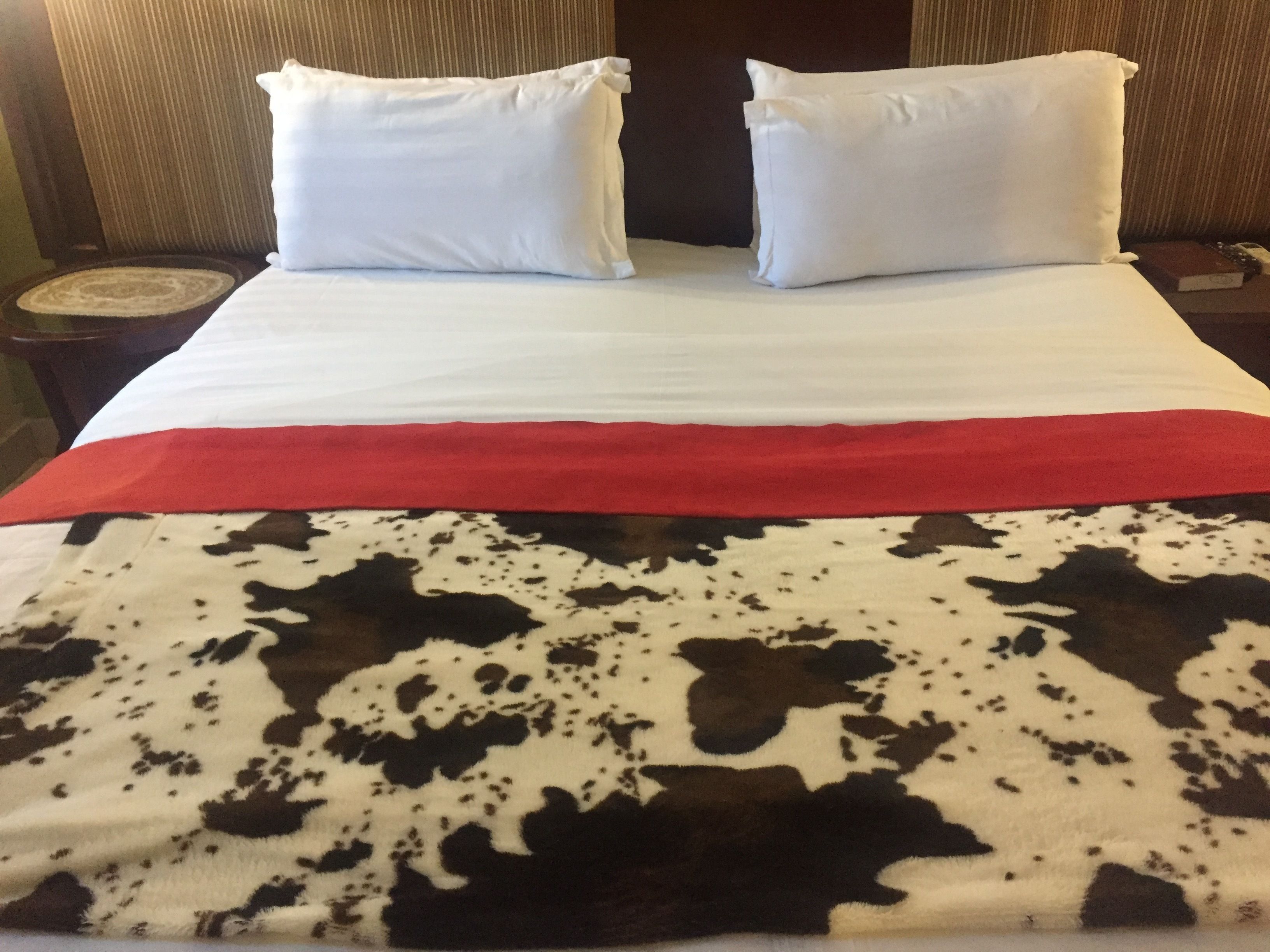 A bed with white pillows, a red blanket, and a cowhide-patterned bedspread.