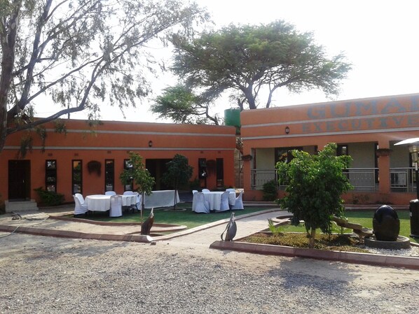 A building with a sign reading "GOMAR EXECUTIVE". There are outdoor tables set up with white tablecloths, and a small garden area with a tree and a birdbath.