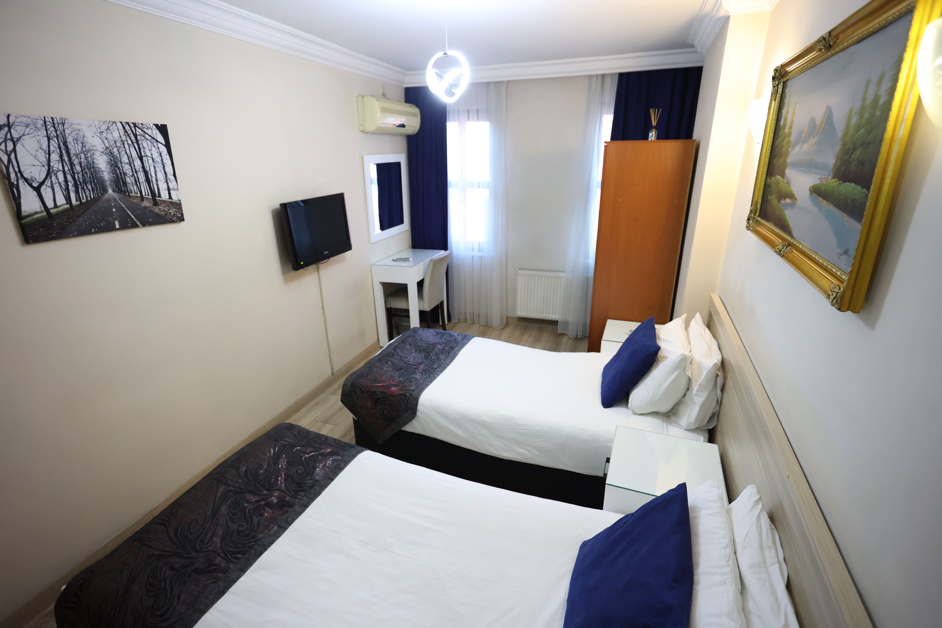 A hotel room with two beds, a desk, a TV, and a painting on the wall.