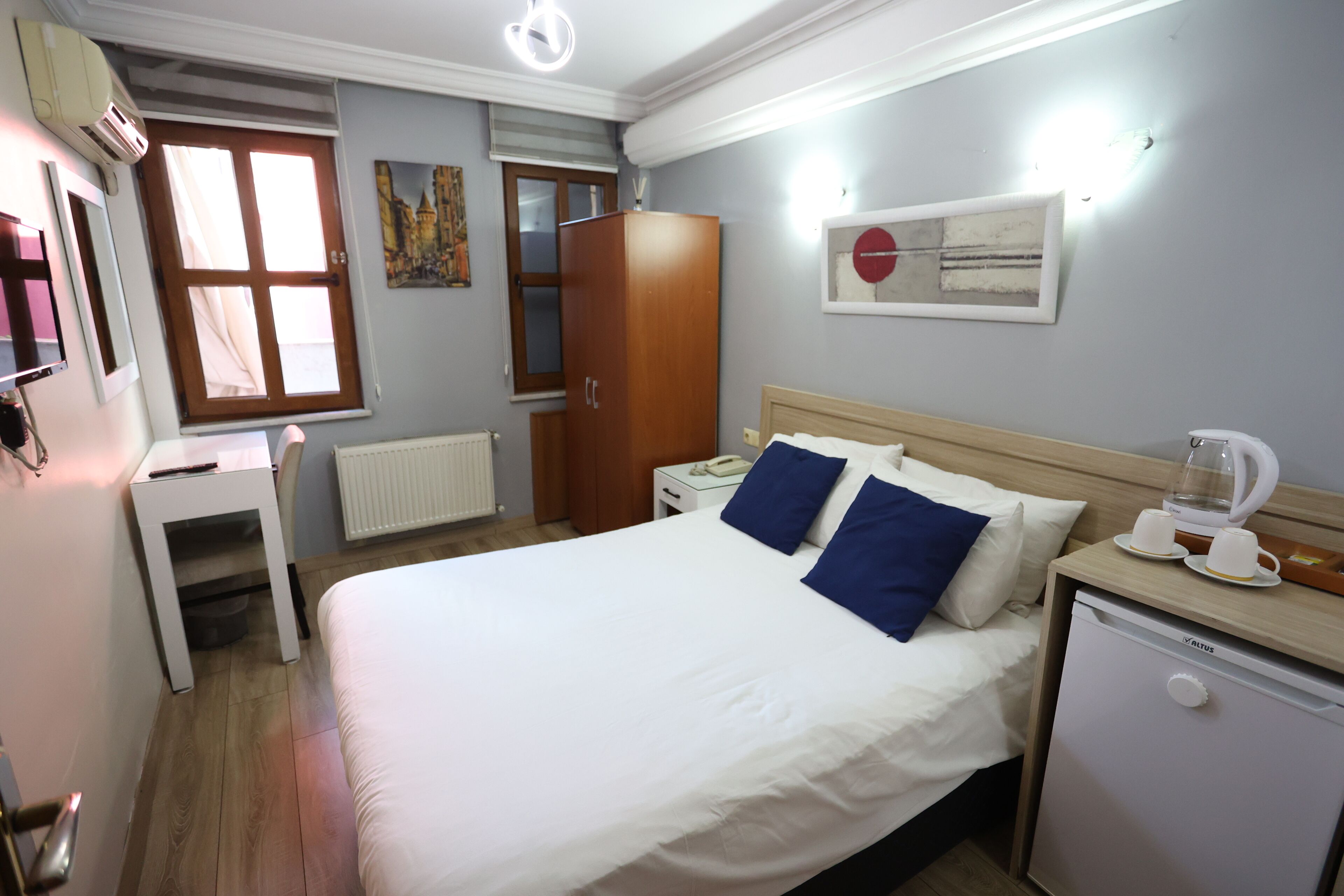 A hotel room with a bed, a desk, a wardrobe, a mini-fridge, and a radiator.