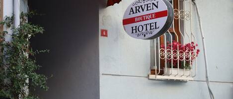 A hotel entrance with a sign reading "Arven Boutique Hotel," a large umbrella, potted plants, and a staircase leading to the entrance.