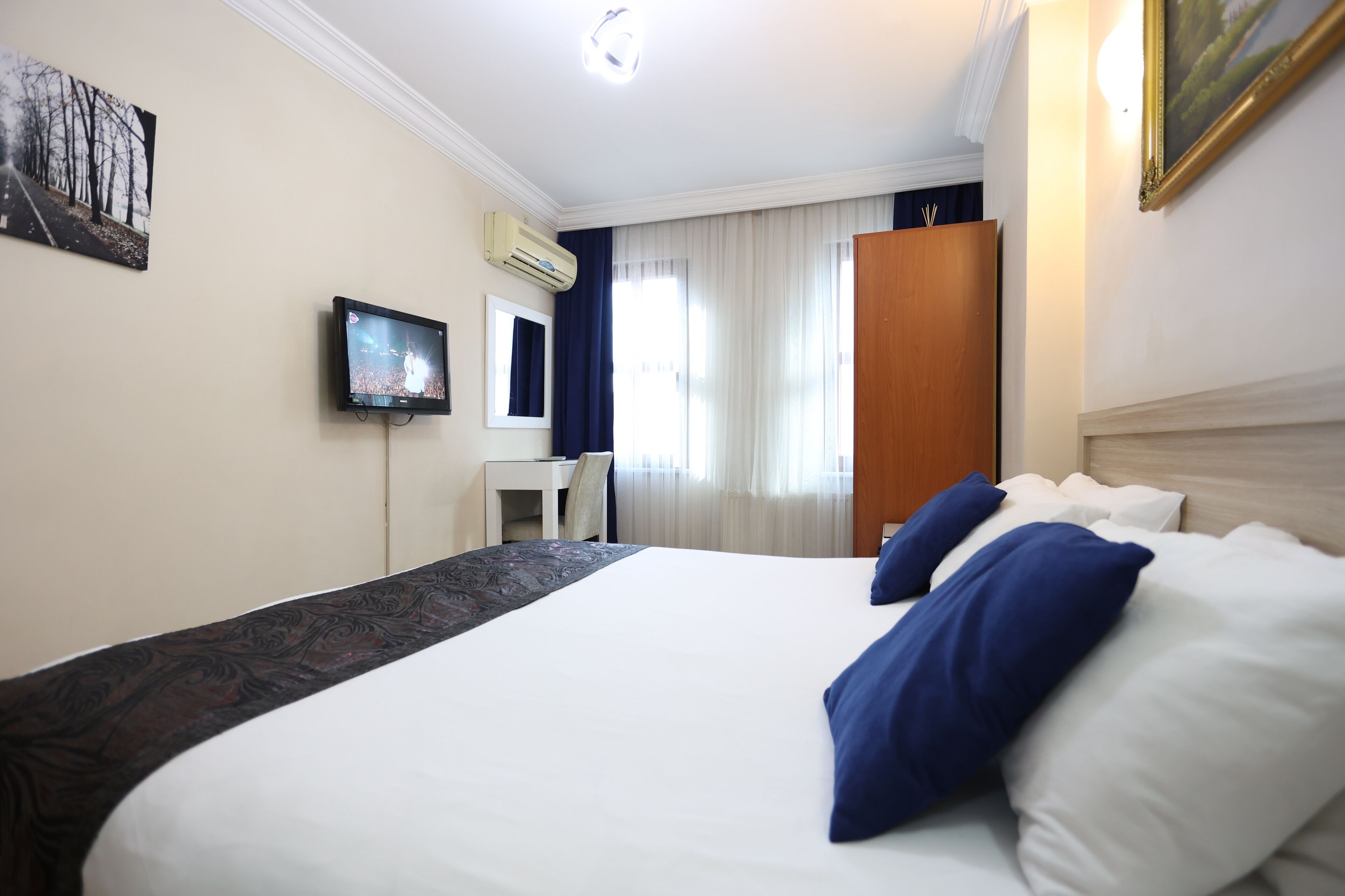 A hotel room with a large bed, a desk, a television, and a window with curtains.