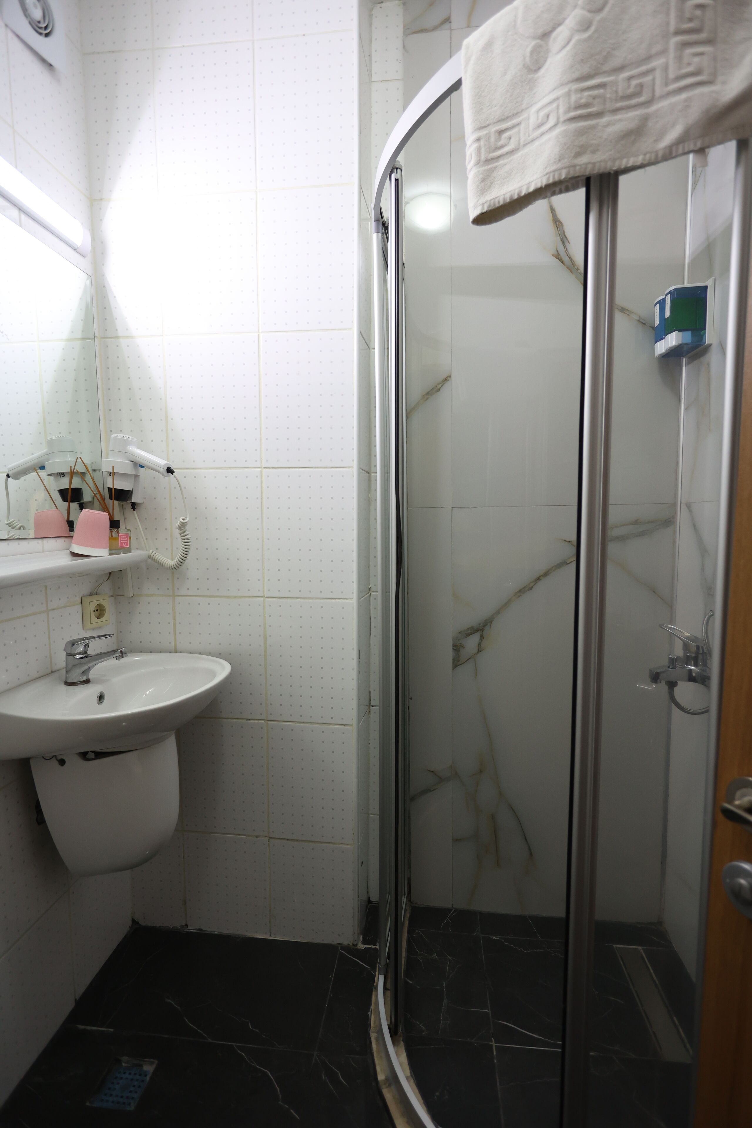 A bathroom with a white sink, a glass shower enclosure, and a marble-tiled floor.