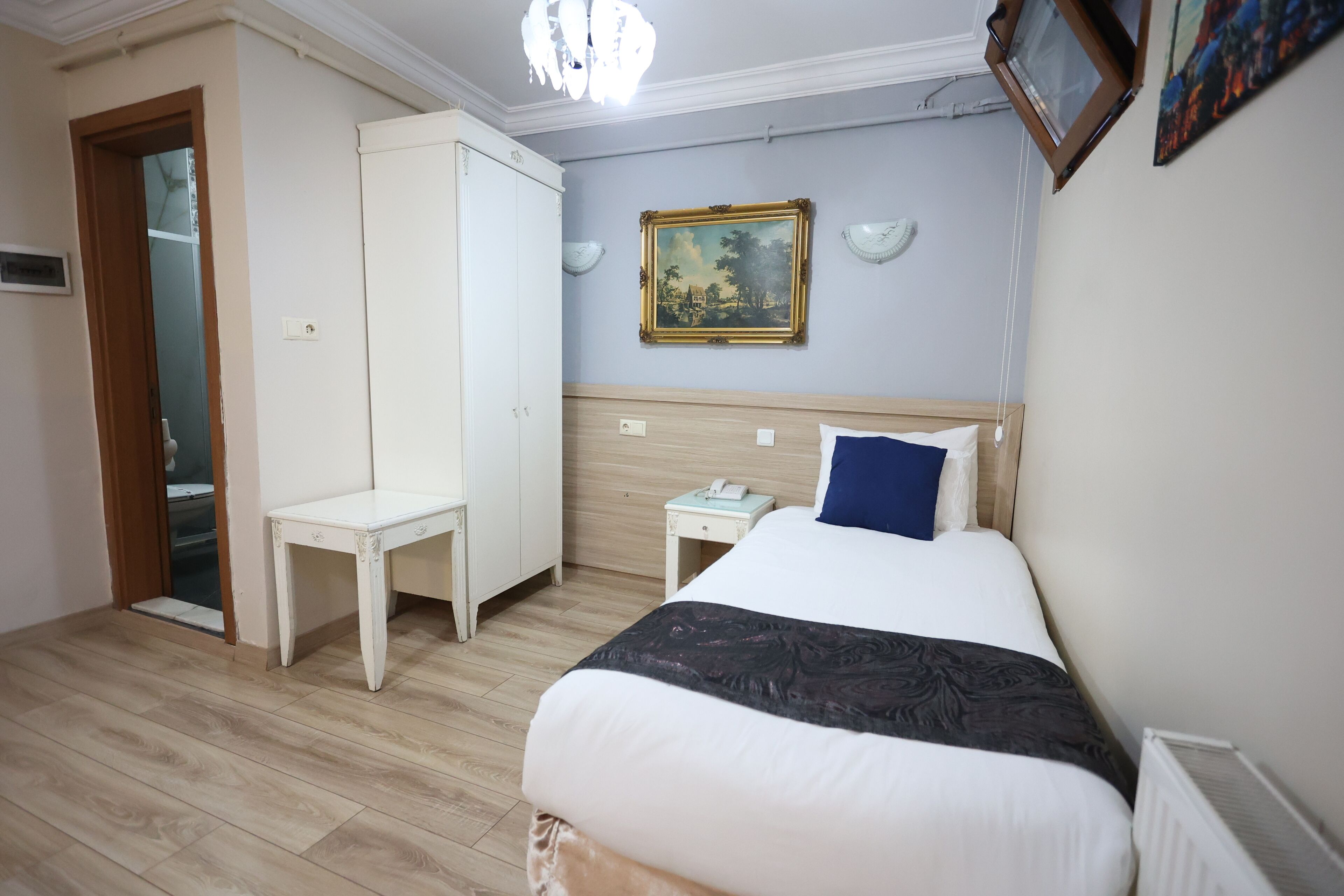 Une chambre à coucher comprenant un lit, un bureau, une armoire, une table de chevet et un tableau accroché au mur.