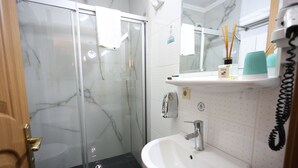 Un baño con cabina de ducha de vidrio, un lavabo blanco y un espejo sobre él.