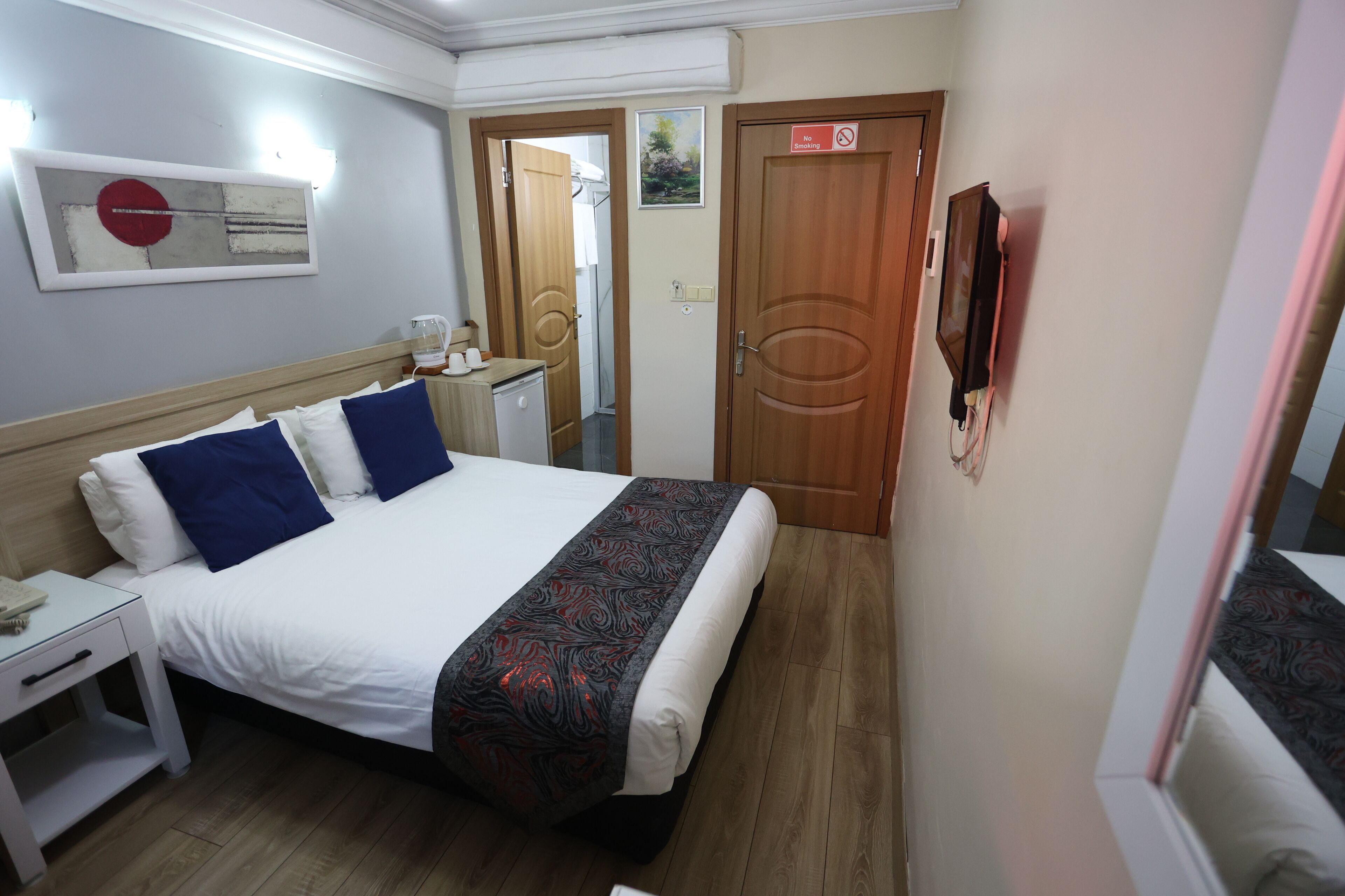 A hotel room with a bed, bedside table, nightstand, and a TV mounted on the wall.