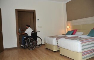 Habitación de hotel con dos camas, una silla de ruedas y una puerta de madera.