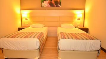 A hotel room with two single beds, wooden headboards, and bedside lamps.