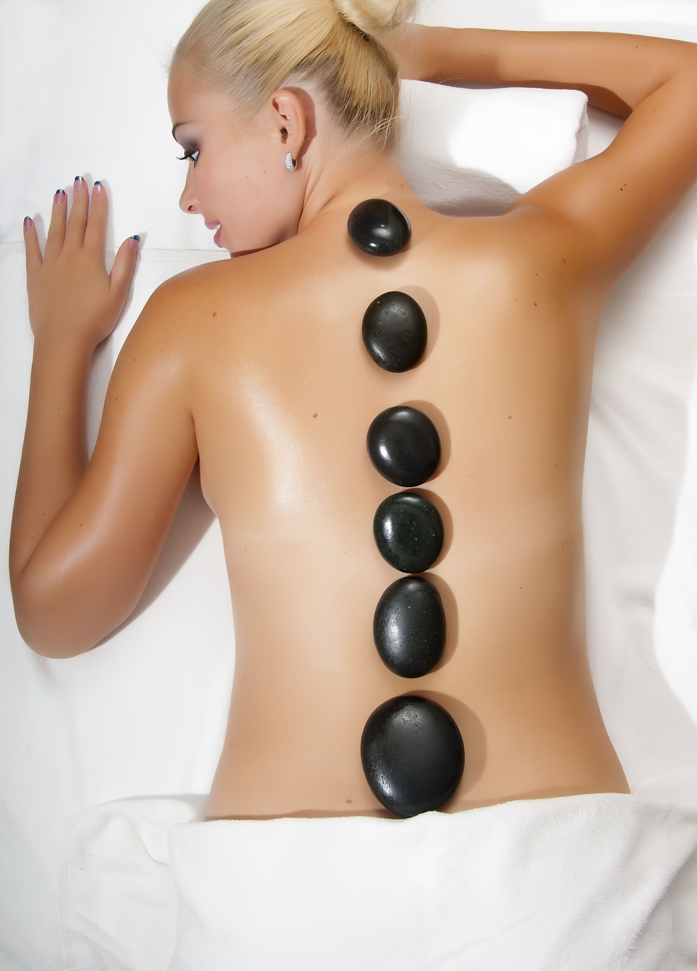A person receiving a back massage with black stones placed along the spine.