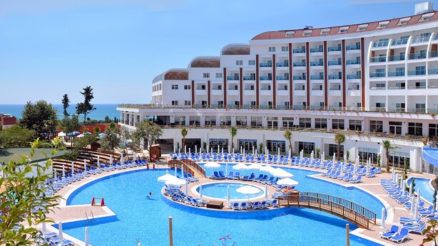 A hotel with a large pool surrounded by sun loungers and umbrellas, a clear view of the ocean, and a modern building with balconies. - Side Prenses Resort Hotel & Spa - All Inclusive (Manavgat)
