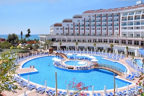 Um hotel com uma piscina grande, cercada por espreguiçadeiras e guarda-sóis, vista clara do oceano e um edifício moderno com varandas.