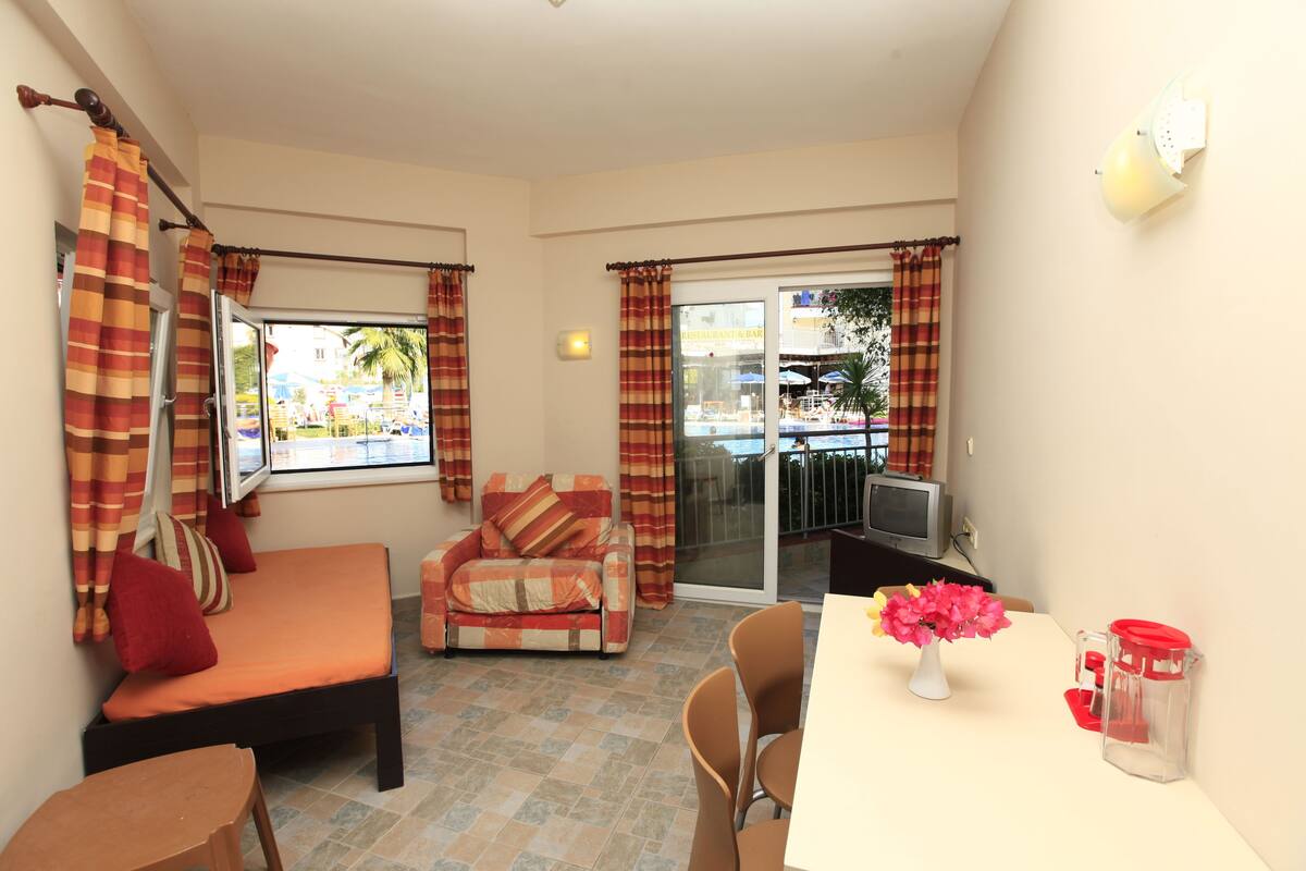 Una habitación con sofá, una mesa de comedor con sillas, televisión y vistas al exterior.