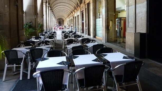 A covered outdoor dining area with rows of tables and chairs, a central walkway, and a view of a building with a sign that reads "HOTEL RO." - Hotel Roma Reial (Barcelona)