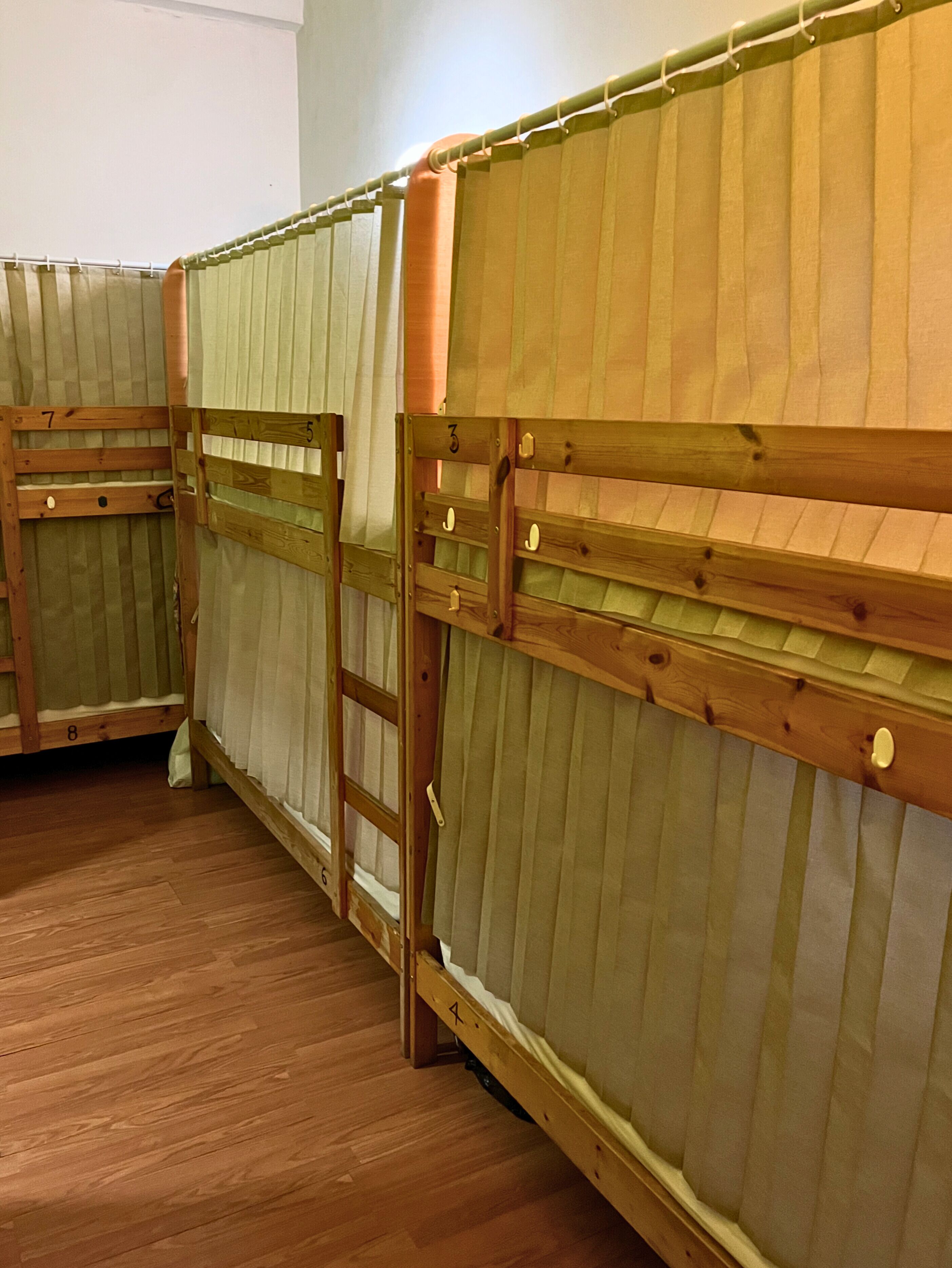 A row of bunk beds with wooden frames and green fabric bedding.