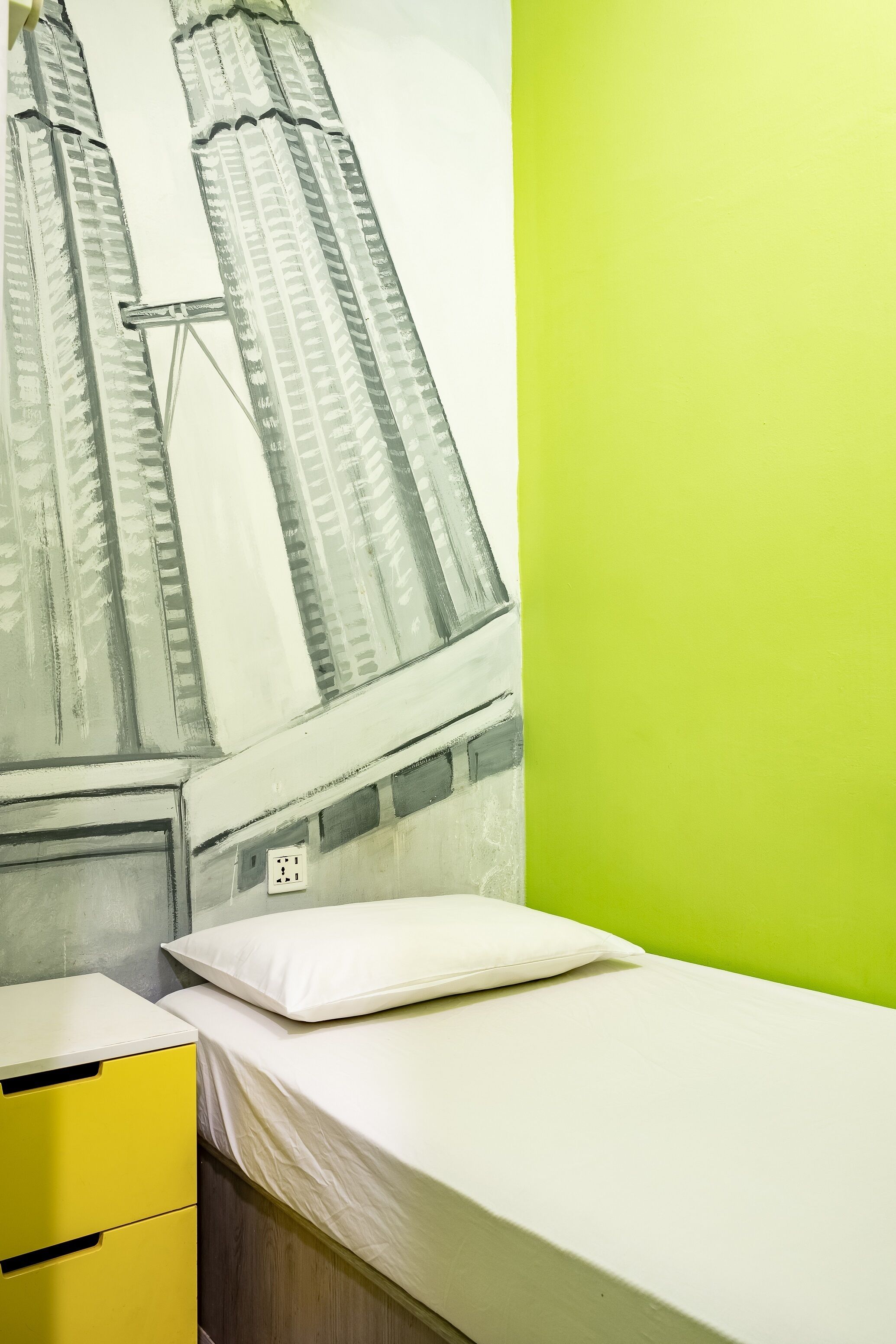 A room with a bed, a yellow dresser, and a wall mural of a bridge.