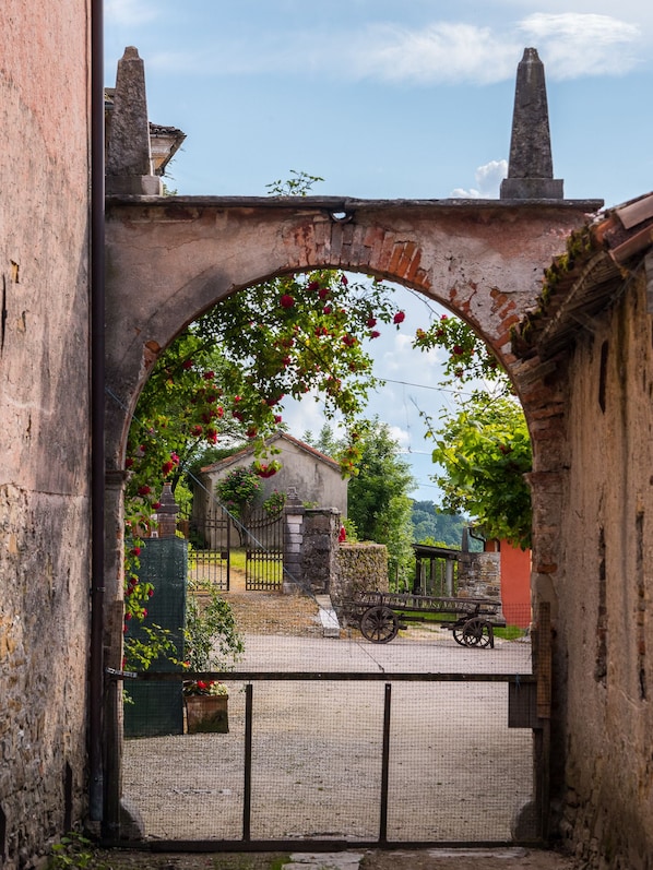 An arched stone gateway with a rustic fence and a cart in the foreground.