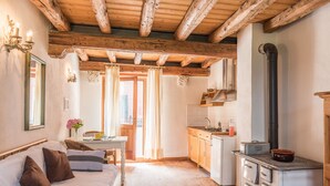 Une pièce chaleureuse avec un plafond en bois, un lit avec des oreillers, une petite table avec un vase et une kitchenette équipée d’une cuisinière et de placards.