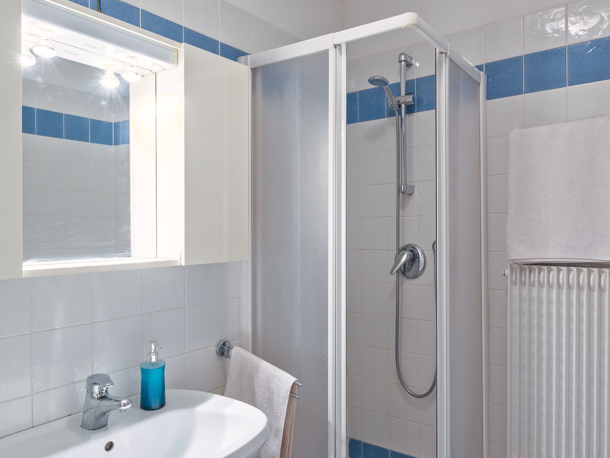 Un baño con ducha, lavamanos y un perchero para toallas.