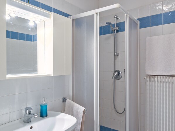 Un baño con ducha, lavamanos y un perchero para toallas.