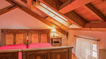 Un dormitorio de madera con techo inclinado, una cama con ropa de cama roja, una mesita de noche, una lámpara y una ventana con cortinas.