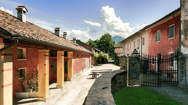 Una estrecha calle adoquinada bordeada por edificios tradicionales con fachadas rojas y amarillas, muros de piedra y una verja.