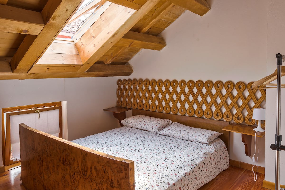 Een slaapkamer met een houten plafond, een bed met een bloemenbedekking, een houten hoofdbord en een nachtkastje.