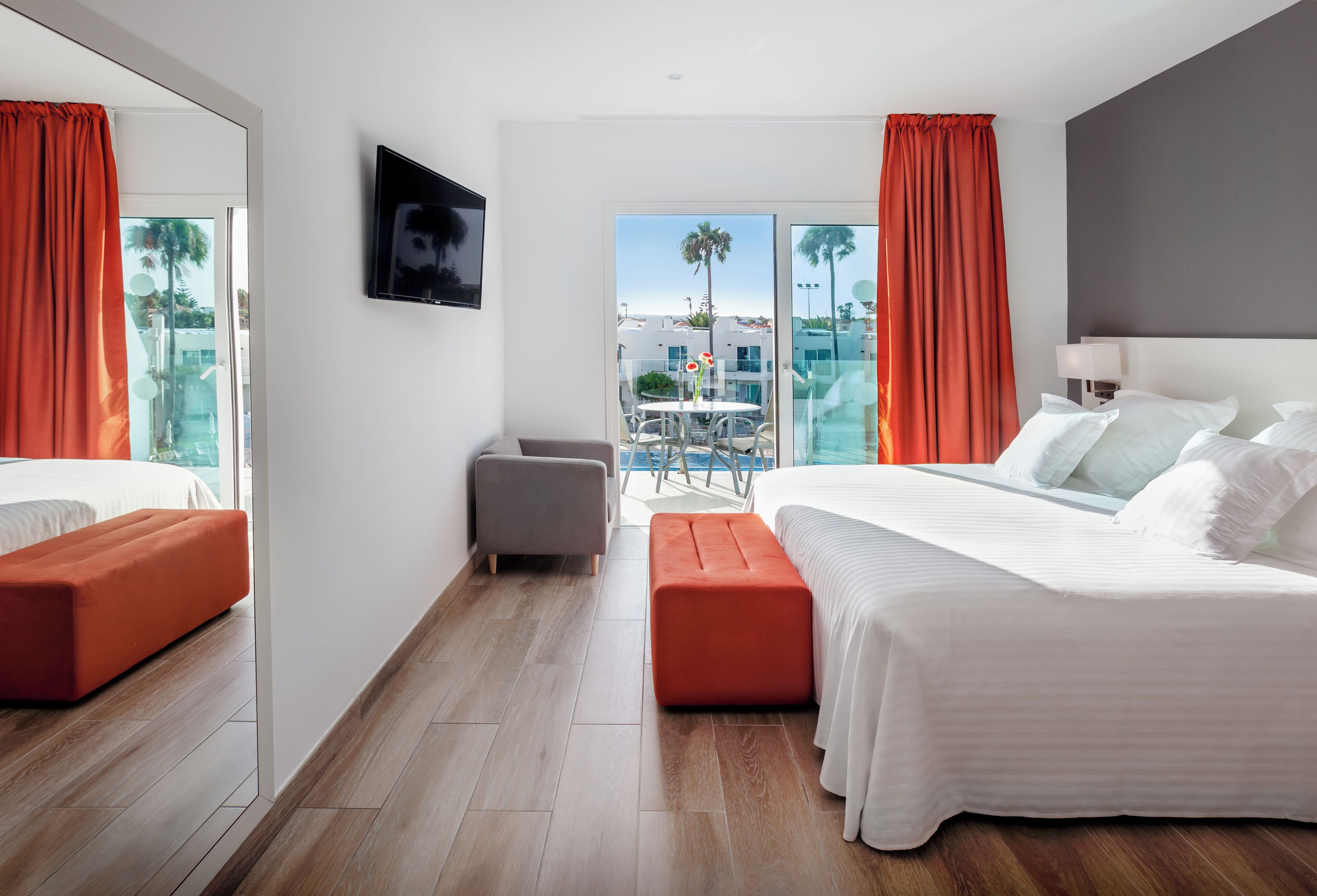 A hotel room with a bed, a seating area, a TV, and a balcony with a view.