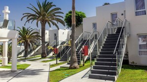 A modern building with a staircase leading to the upper floors, surrounded by palm trees and a clear sky. - Barceló Corralejo Sands (La Oliva)