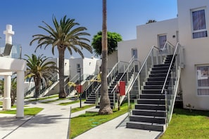 A modern building with a staircase leading to the upper floors, surrounded by palm trees and a clear sky. - Barceló Corralejo Sands (La Oliva)