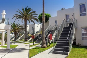 Un edificio moderno con una escalera que conduce a los pisos superiores, rodeado de palmeras y un cielo despejado.