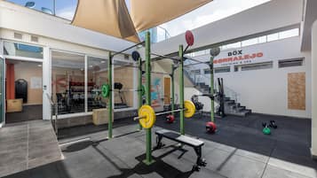 Un área de gimnasio al aire libre con una estación de levantamiento de pesas, pelotas de ejercicio y una escalera que conduce a un nivel superior.