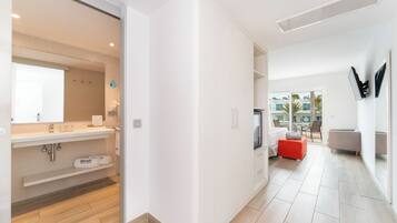 Habitación de hotel moderna con baño, zona de estar con un reposapiés rojo y un amplio ventanal con vistas al exterior.