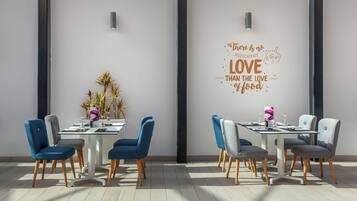 Een eetgedeelte met twee tafels, elk omringd door stoelen. Op de tafels staan decoratieve planten en aan de muur hangt een inspirerende quote.