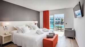 Habitació d'hotel moderna amb un llit gran, un otomà taronja petit, una butaca gris i un balcó amb vista a la piscina.