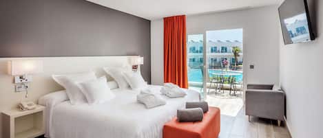 A modern hotel room with a large bed, a small orange ottoman, a grey armchair, and a balcony with a pool view.