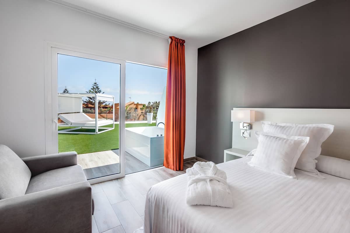 Una moderna camera d'albergo con un letto grande, un'area salotto e vista sulla piscina e sugli spazi esterni.