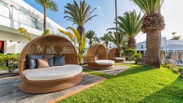 Outdoor wicker lounge chairs with cushions, palm trees, and a modern building in the background.