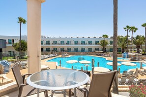 Zona de piscina con sillones, sombrillas y una mesa de vidrio.