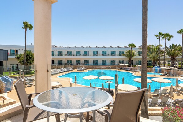A poolside area with lounge chairs, umbrellas, and a glass table. - Barceló Corralejo Sands (La Oliva)