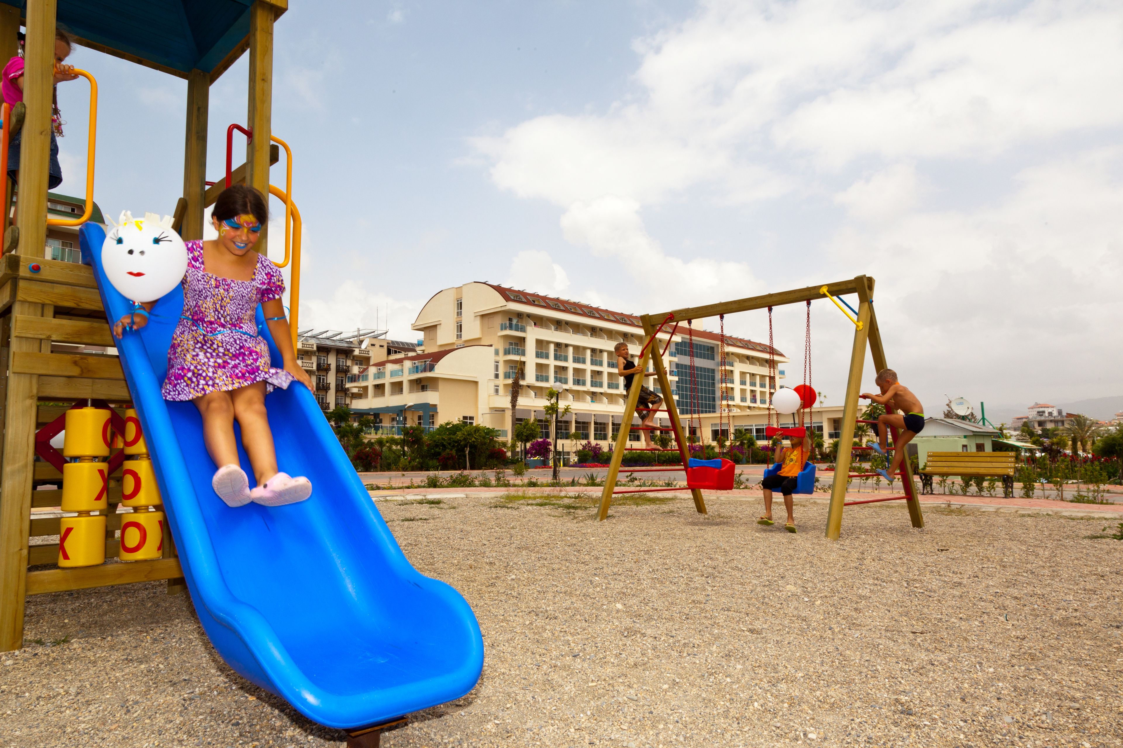 Ein Spielplatz mit einer blauen Rutsche, Schaukeln und einem Gebäude im Hintergrund.