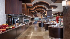 Un hall d’hôtel moderne avec un long comptoir d’accueil, un grand espace buffet proposant une variété de plats et une composition florale décorative.