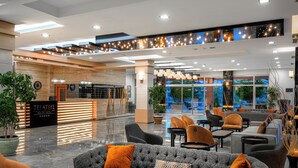 Un hall d’hôtel moderne doté d’un comptoir d’accueil, d’espaces détente et de grandes fenêtres offrant une vue sur l’extérieur.