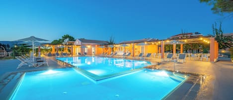 Ein Schwimmbecken mit Liegestühlen und Sonnenschirmen, umgeben von Gebäuden mit Außenbereich.