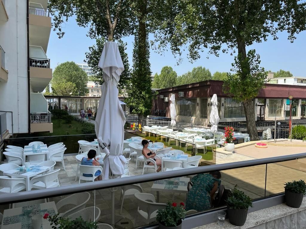 Ein Essbereich im Freien mit weißen Tischen und Stühlen, Sonnenschirmen und Pflanzkübeln.