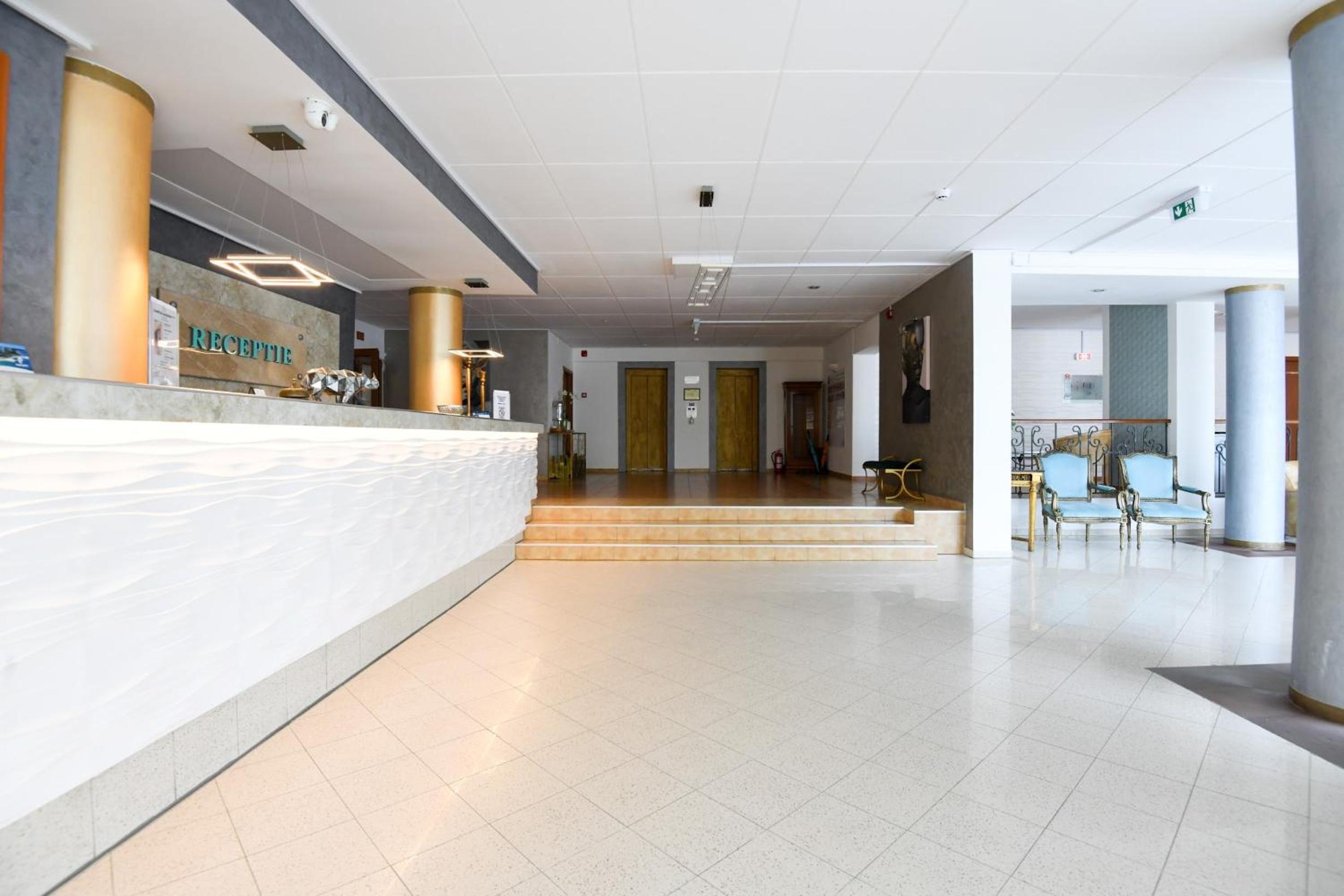 Ein Hotel-Empfangsbereich mit Empfangsschalter, Hinweisschild und einer Treppe zum Obergeschoss.