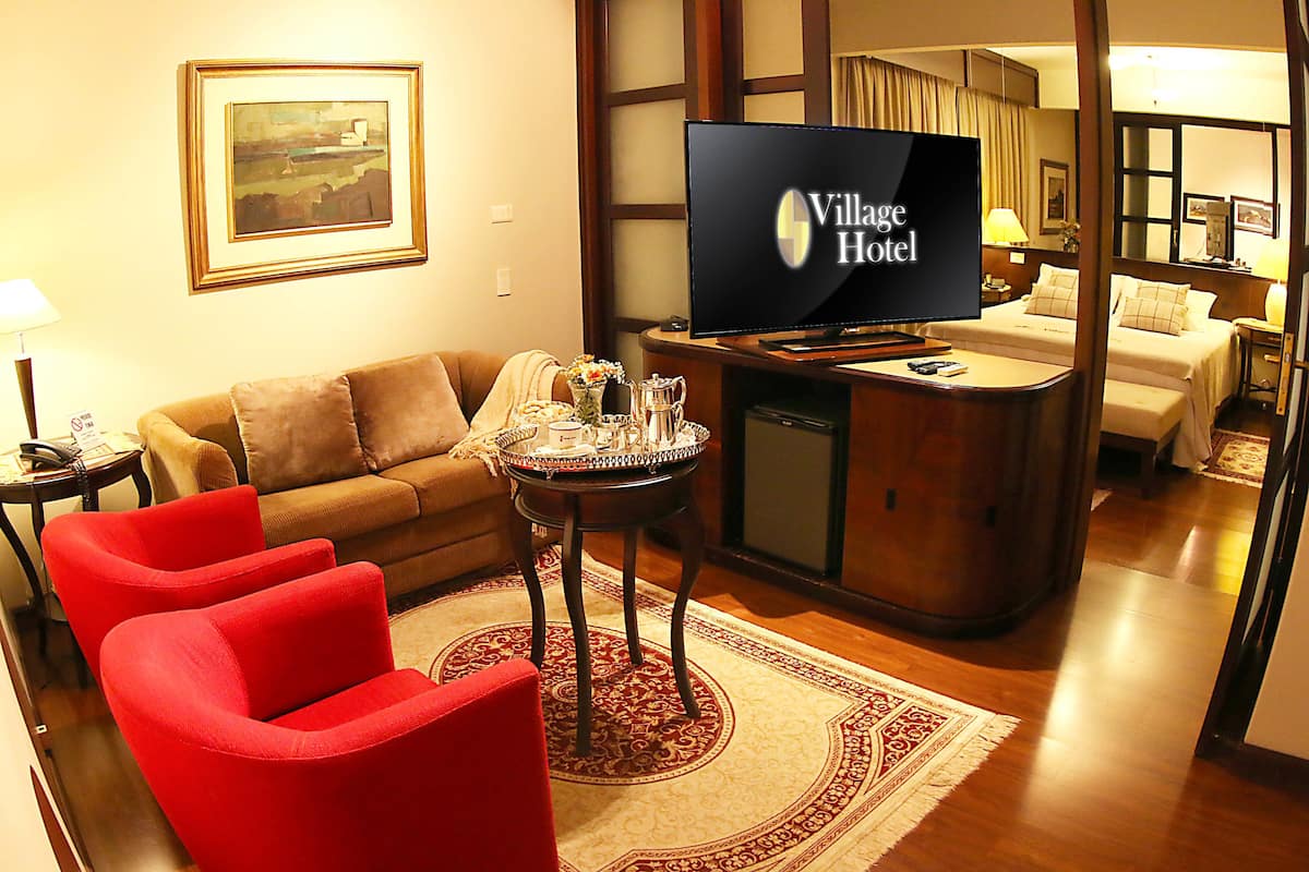 A hotel room with a sofa, red chairs, a TV, a small table with a tray, and a bed.