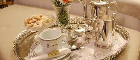 Bandeja de desayuno con tetera, tazas, platillos y un bol de pasteles en una habitación de hotel.