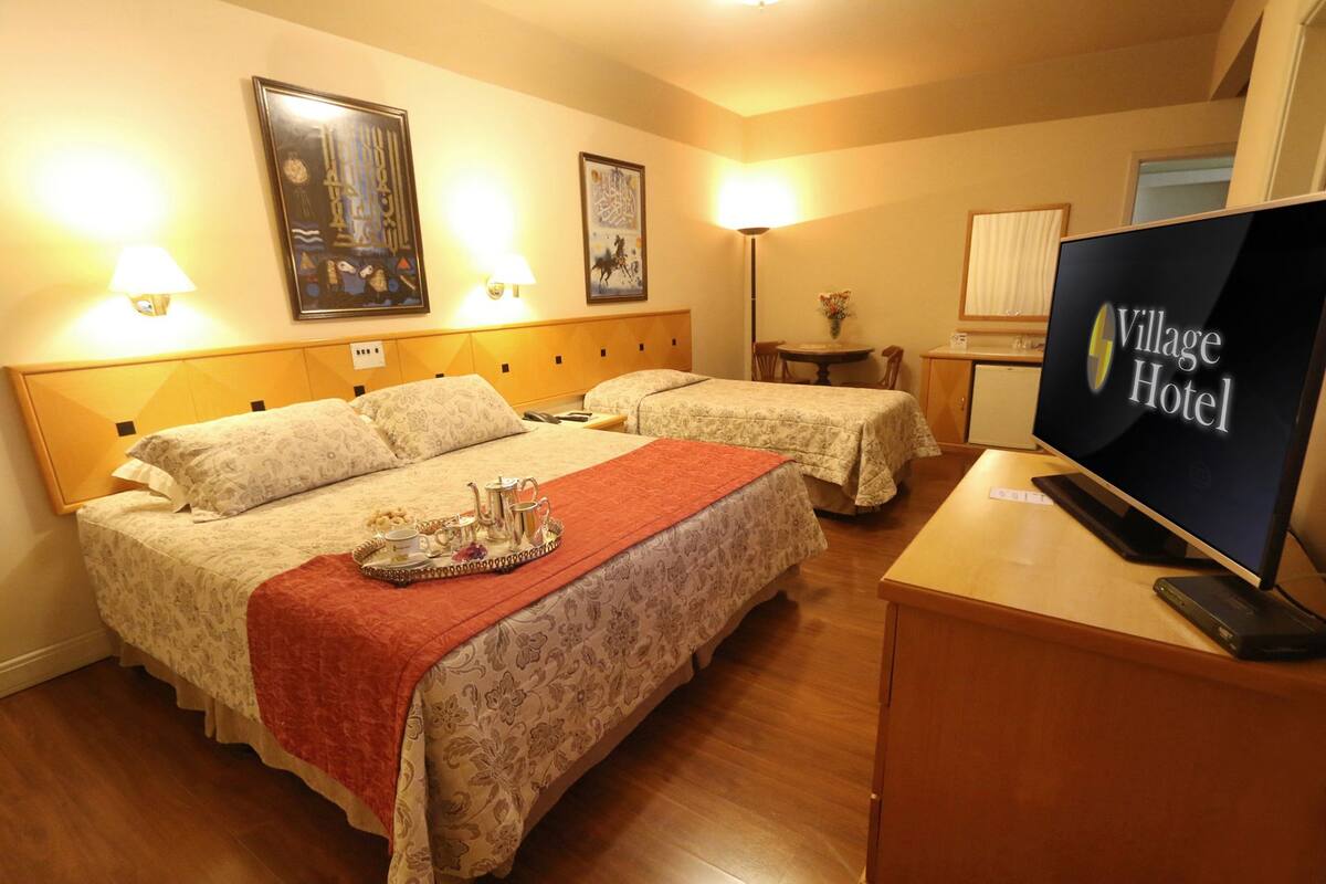 A hotel room with two beds, a TV, and artwork on the walls.